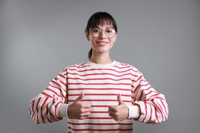 Photo of Happy woman showing thumbs up on grey background. Like gesture