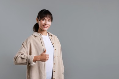 Photo of Happy woman showing thumbs up on grey background, space for text. Like gesture