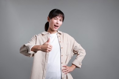 Photo of Woman showing thumbs up on grey background. Like gesture