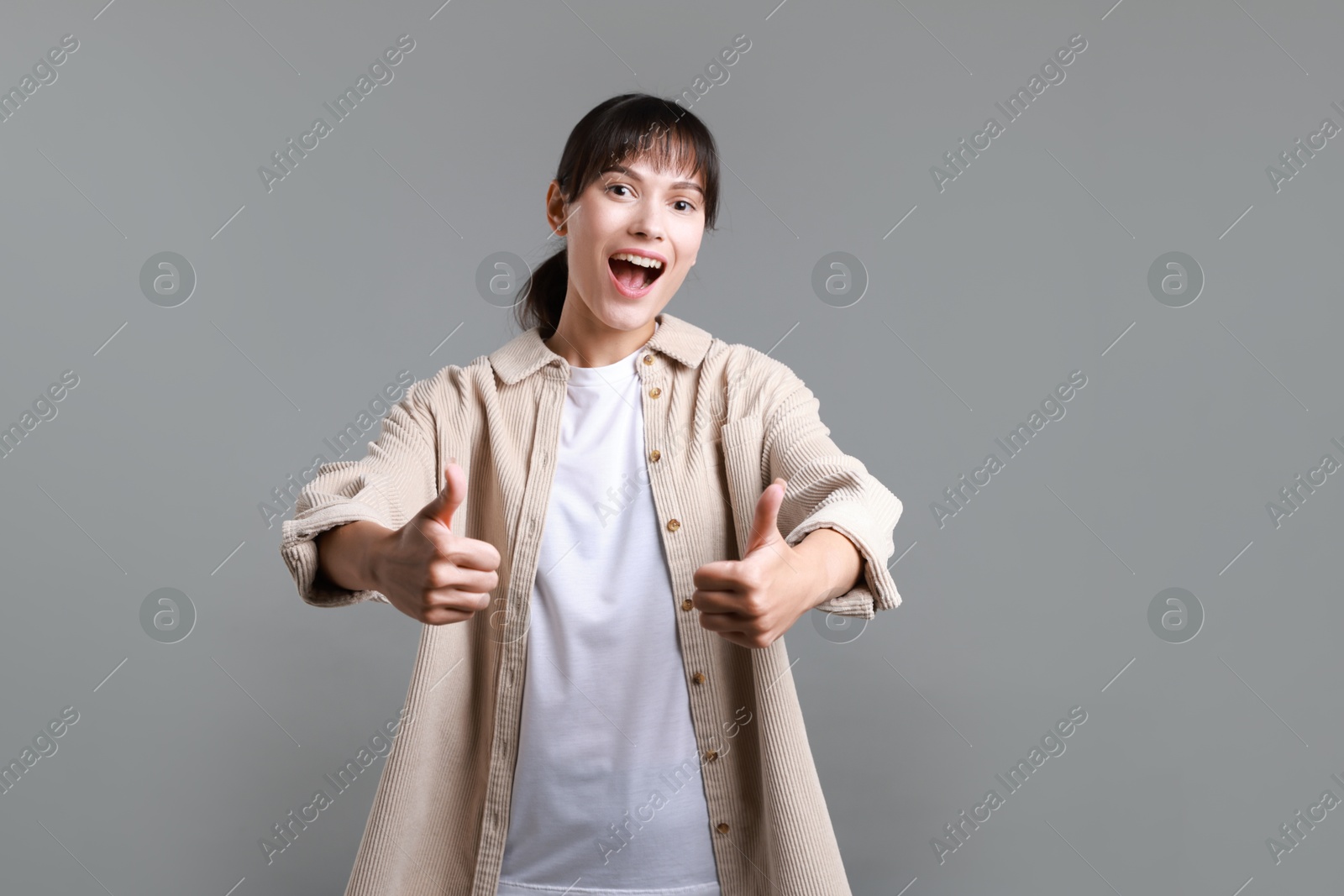 Photo of Happy woman showing thumbs up on grey background. Like gesture