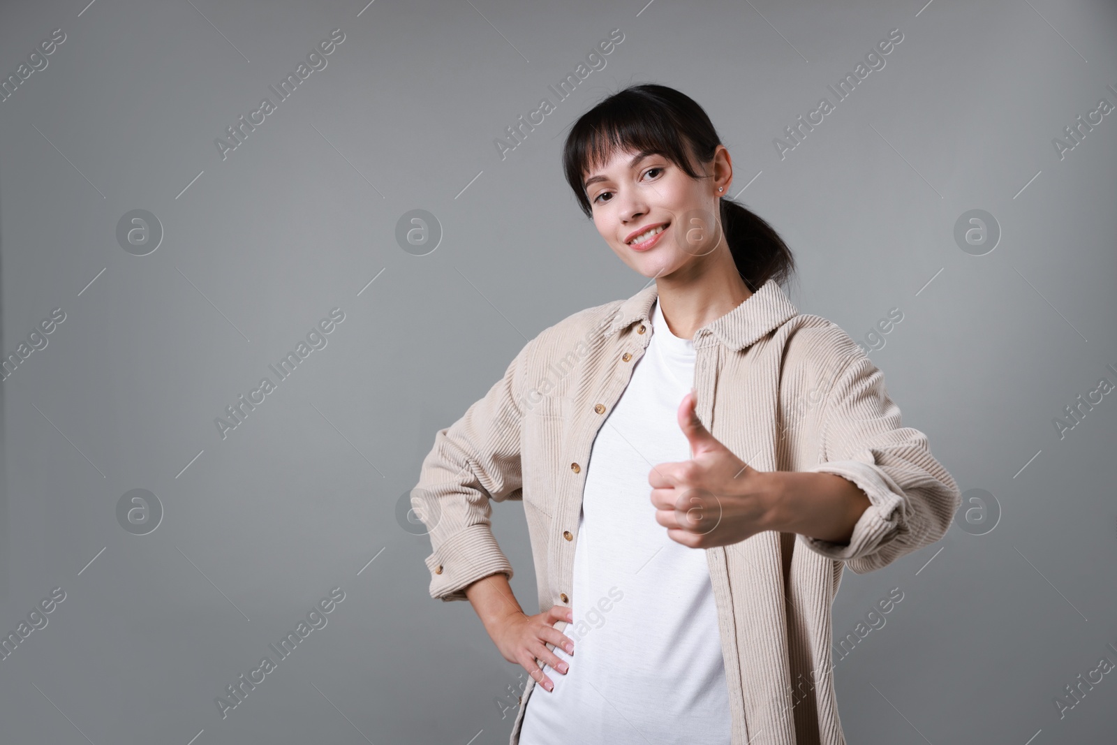 Photo of Happy woman showing thumbs up on grey background, space for text. Like gesture