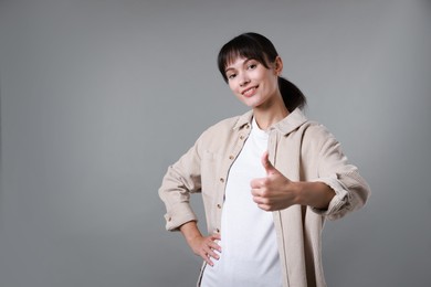 Happy woman showing thumbs up on grey background, space for text. Like gesture