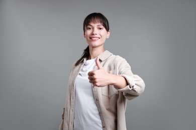 Photo of Happy woman showing thumbs up on grey background. Like gesture