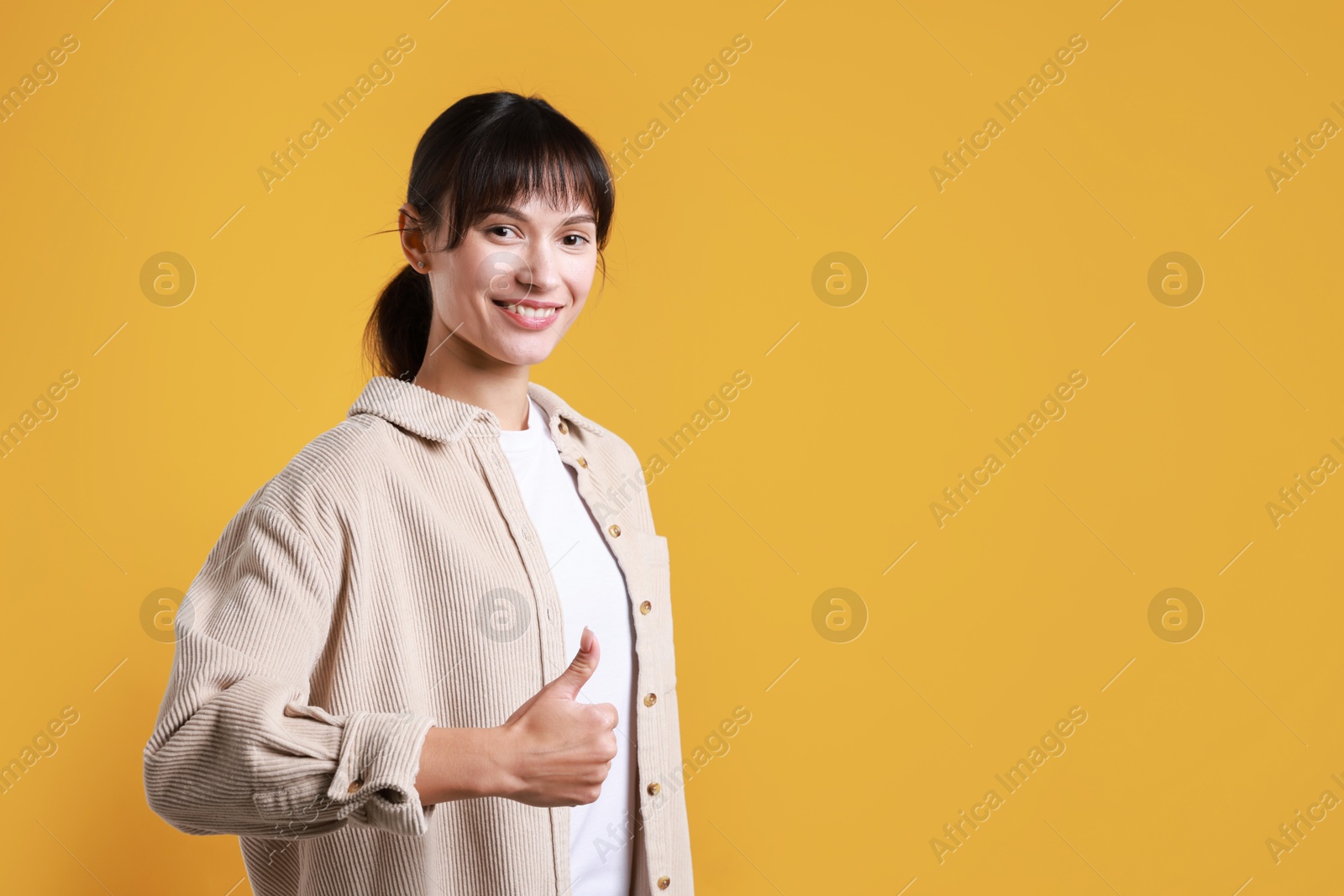 Photo of Happy woman showing thumbs up on orange background, space for text. Like gesture