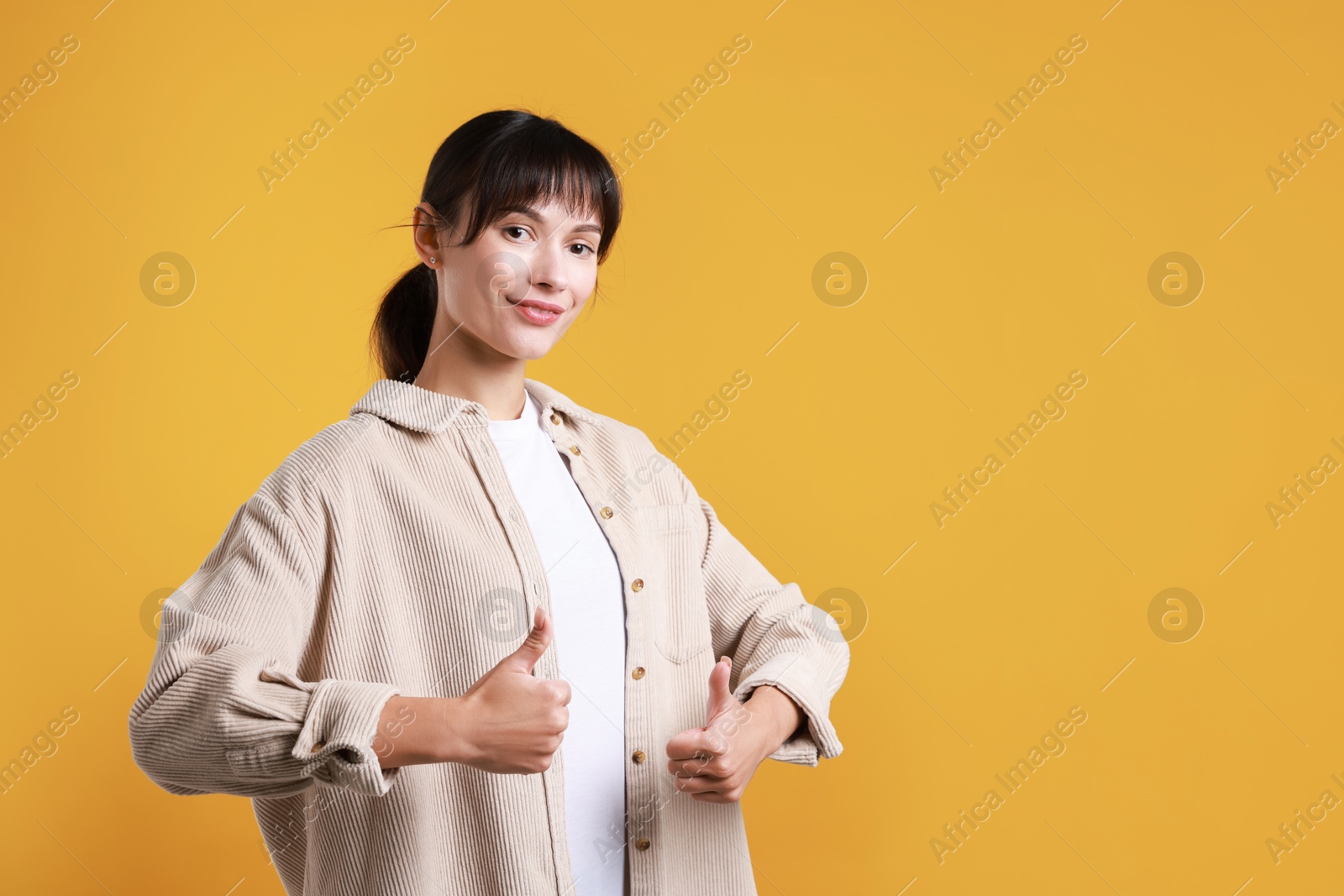 Photo of Happy woman showing thumbs up on orange background, space for text. Like gesture