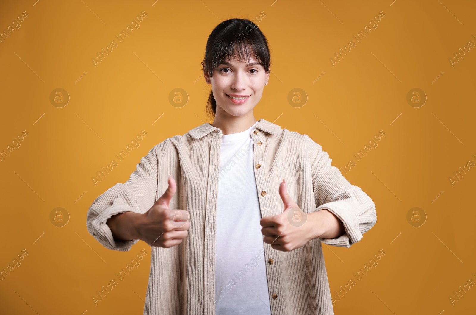 Photo of Happy woman showing thumbs up on orange background. Like gesture