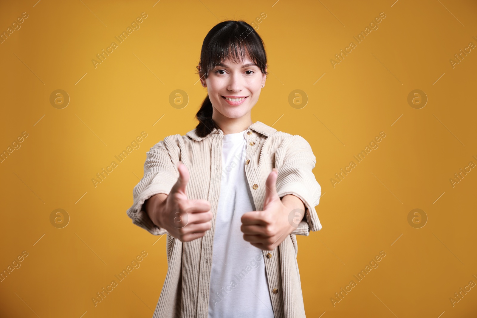 Photo of Happy woman showing thumbs up on orange background. Like gesture