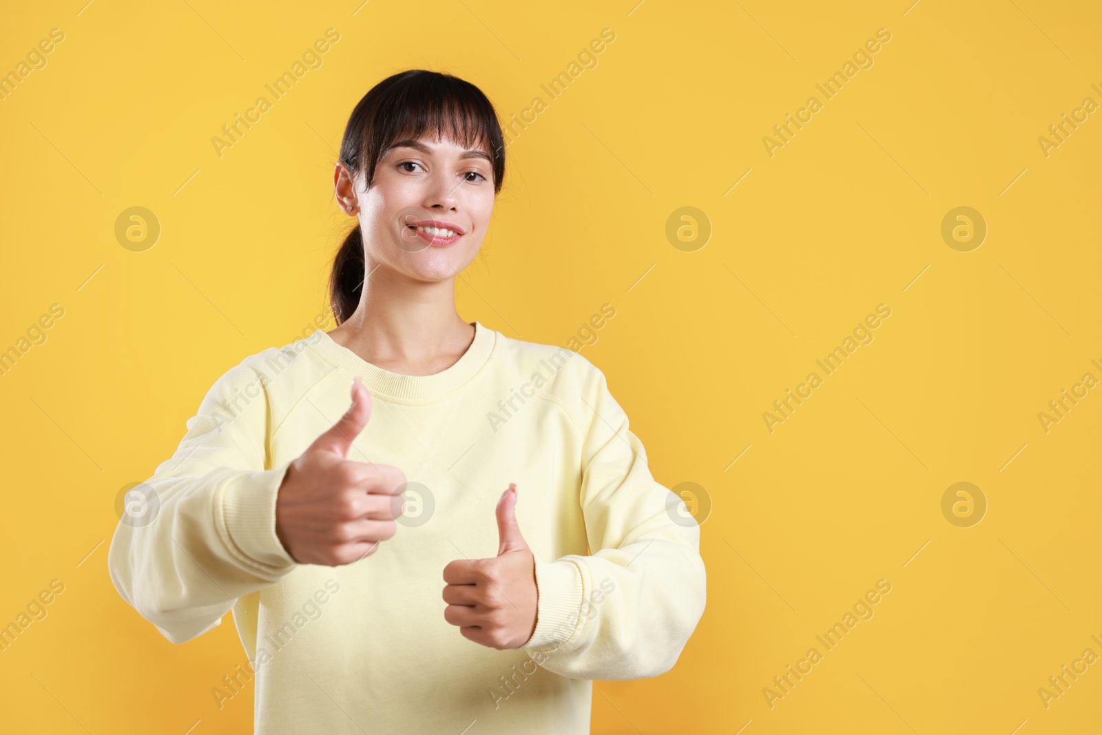 Photo of Happy woman showing thumbs up on orange background, space for text. Like gesture