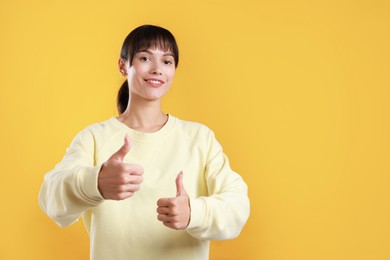 Photo of Happy woman showing thumbs up on orange background, space for text. Like gesture