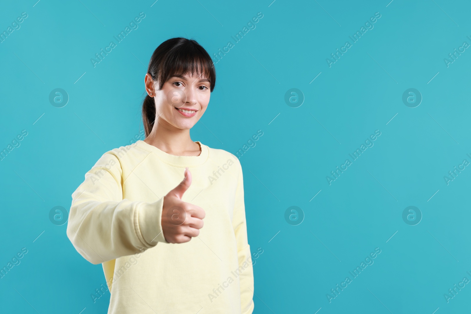 Photo of Happy woman showing thumbs up on light blue background, space for text. Like gesture