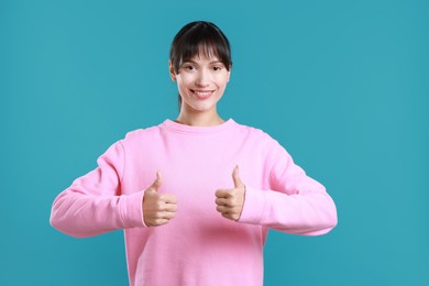 Photo of Happy woman showing thumbs up on light blue background. Like gesture