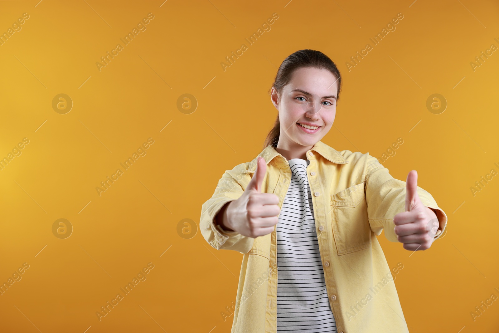 Photo of Happy woman showing thumbs up on orange background, space for text. Like gesture