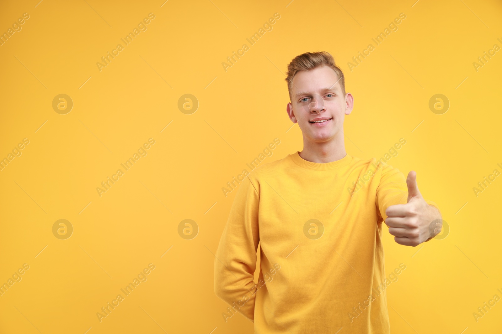 Photo of Happy man showing thumbs up on yellow background, space for text. Like gesture