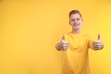 Photo of Happy man showing thumbs up on yellow background, space for text. Like gesture