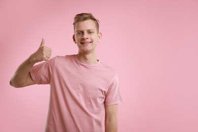 Photo of Happy man showing thumbs up on pink background, space for text. Like gesture