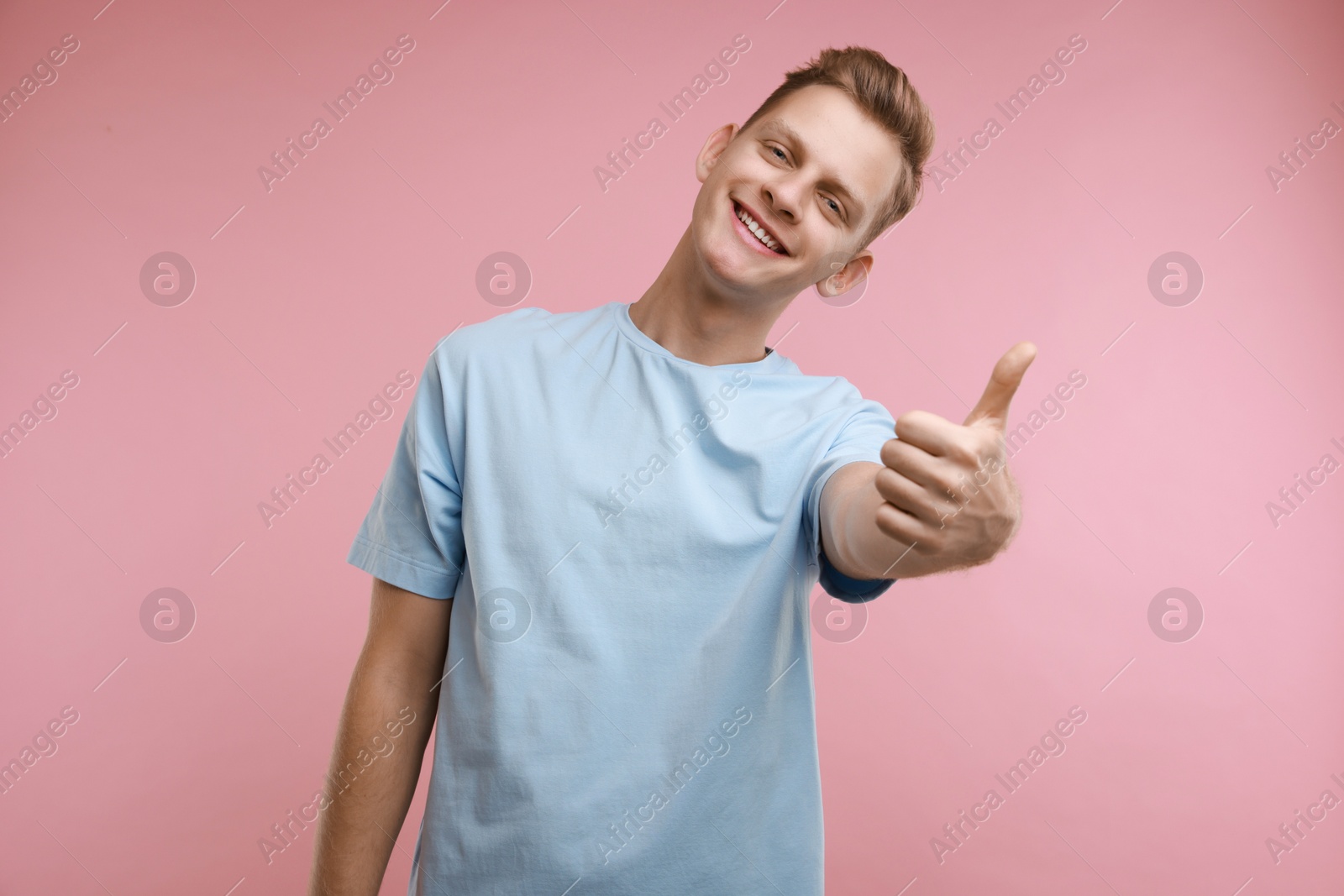 Photo of Happy man showing thumbs up on pink background. Like gesture