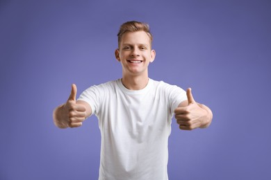 Photo of Happy man showing thumbs up on purple background. Like gesture