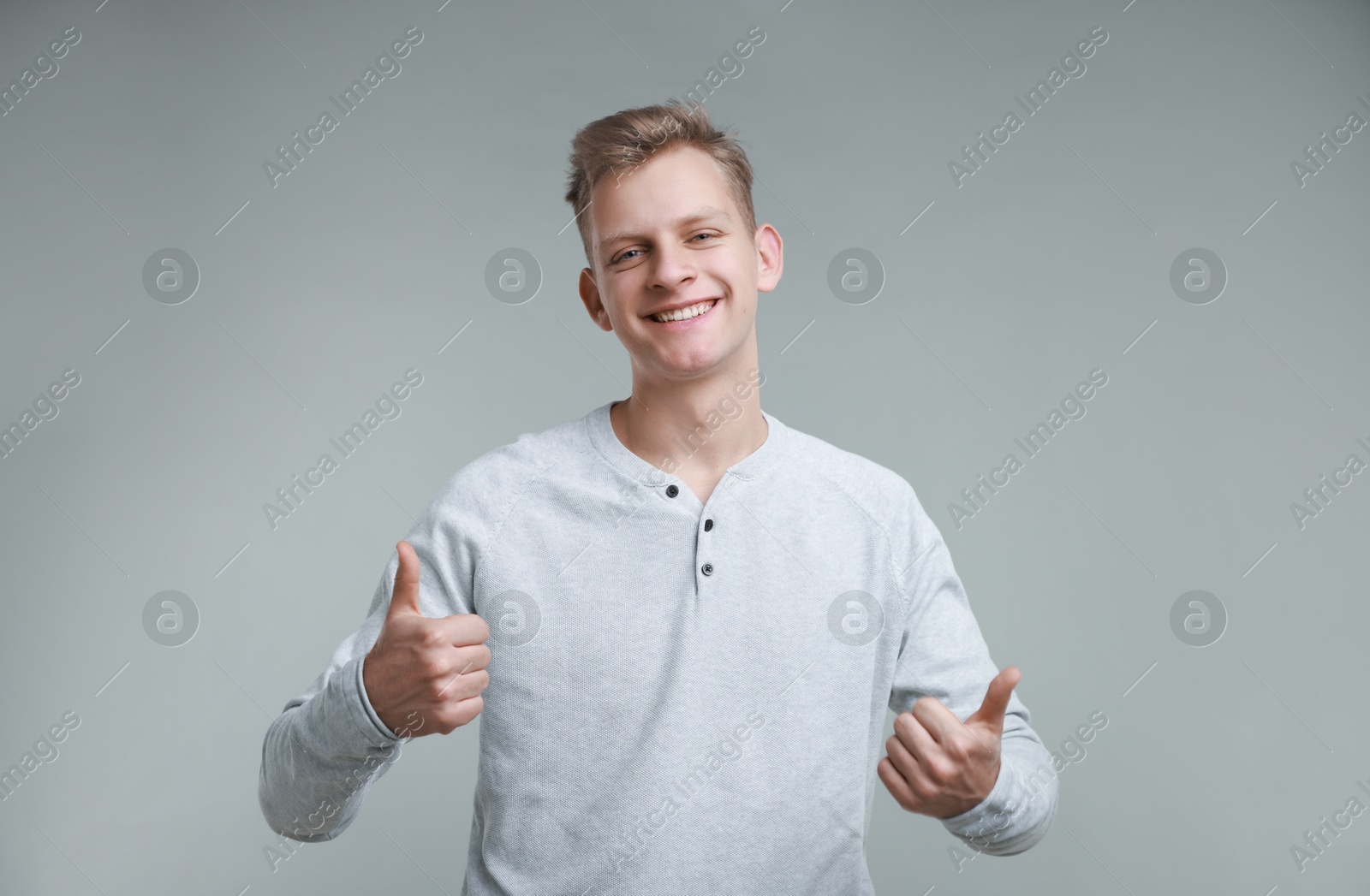 Photo of Happy man showing thumbs up on grey background. Like gesture