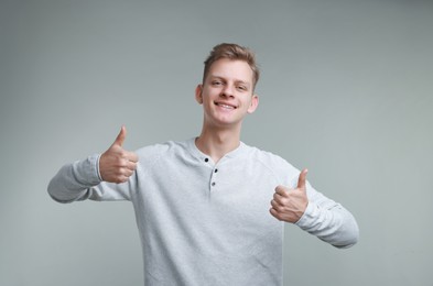 Photo of Happy man showing thumbs up on grey background. Like gesture