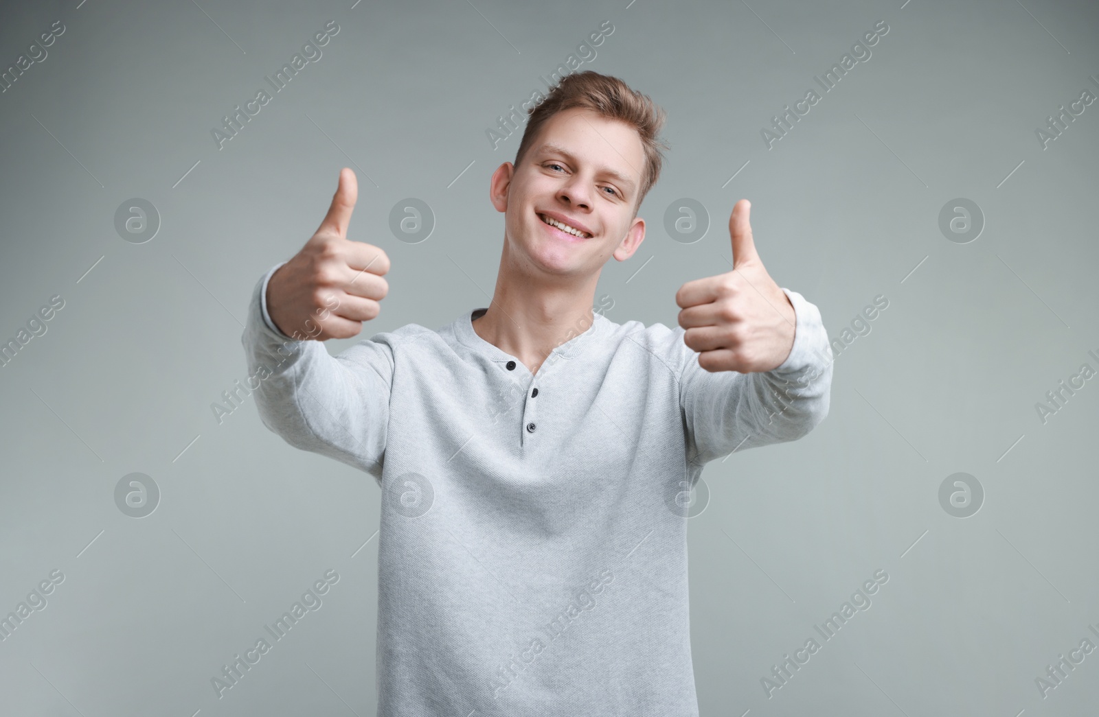 Photo of Happy man showing thumbs up on grey background. Like gesture