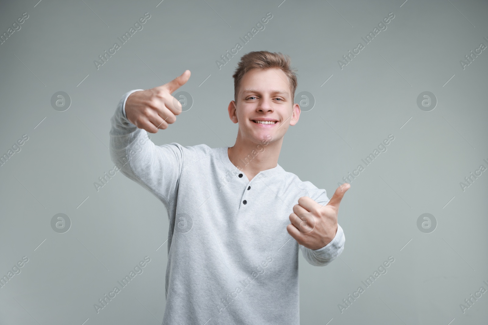 Photo of Happy man showing thumbs up on grey background. Like gesture