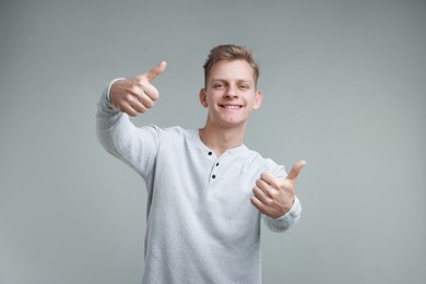 Photo of Happy man showing thumbs up on grey background. Like gesture