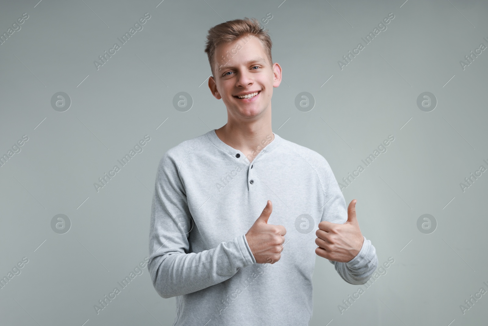 Photo of Happy man showing thumbs up on grey background, space for text. Like gesture