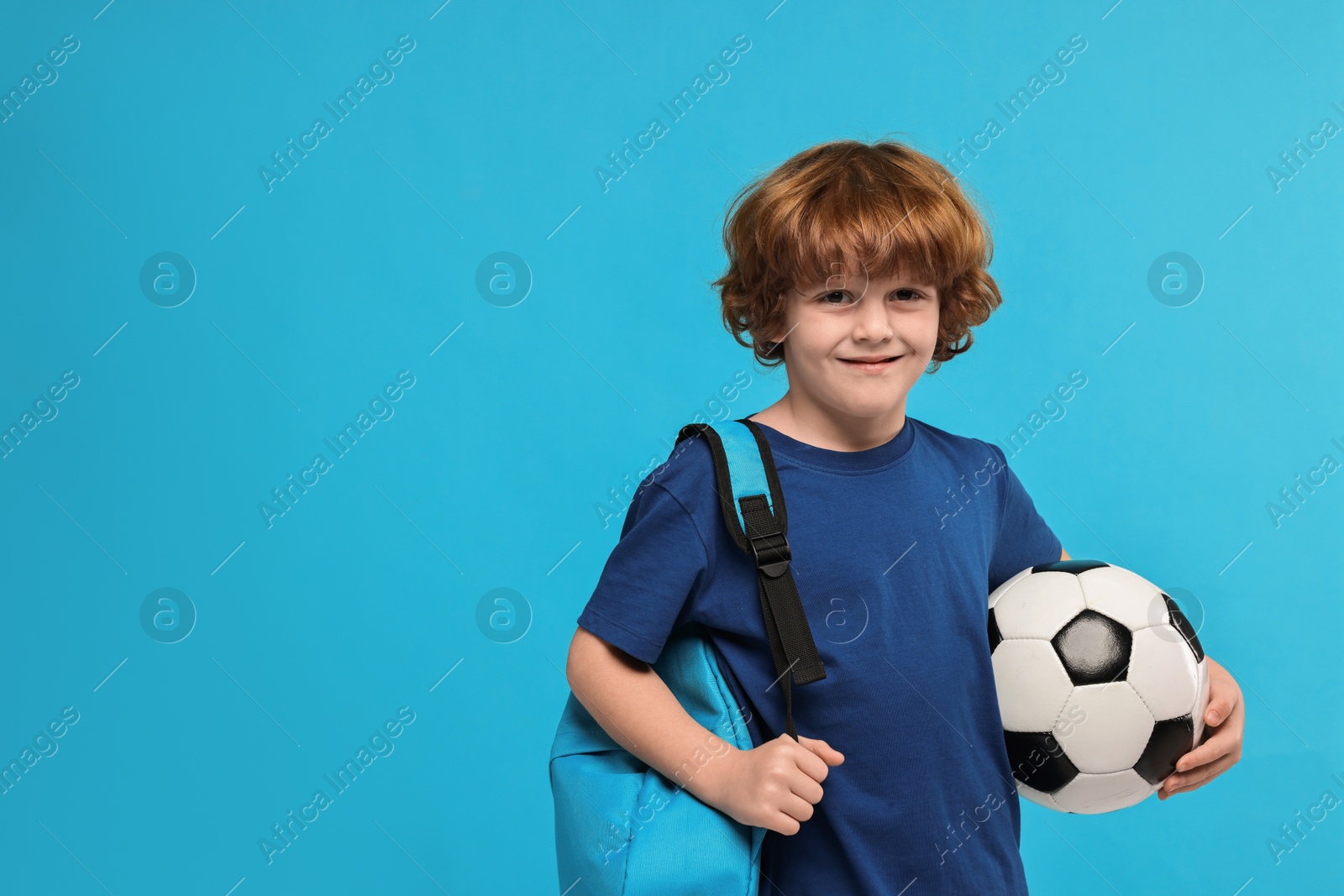 Photo of Little boy with soccer ball and backpack on light blue background, space for text