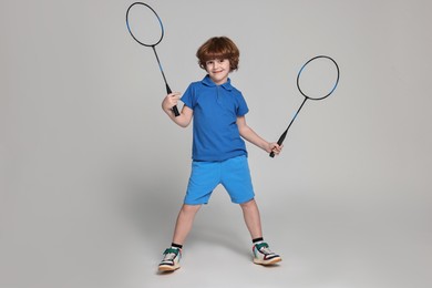 Photo of Little boy with badminton rackets on light grey background