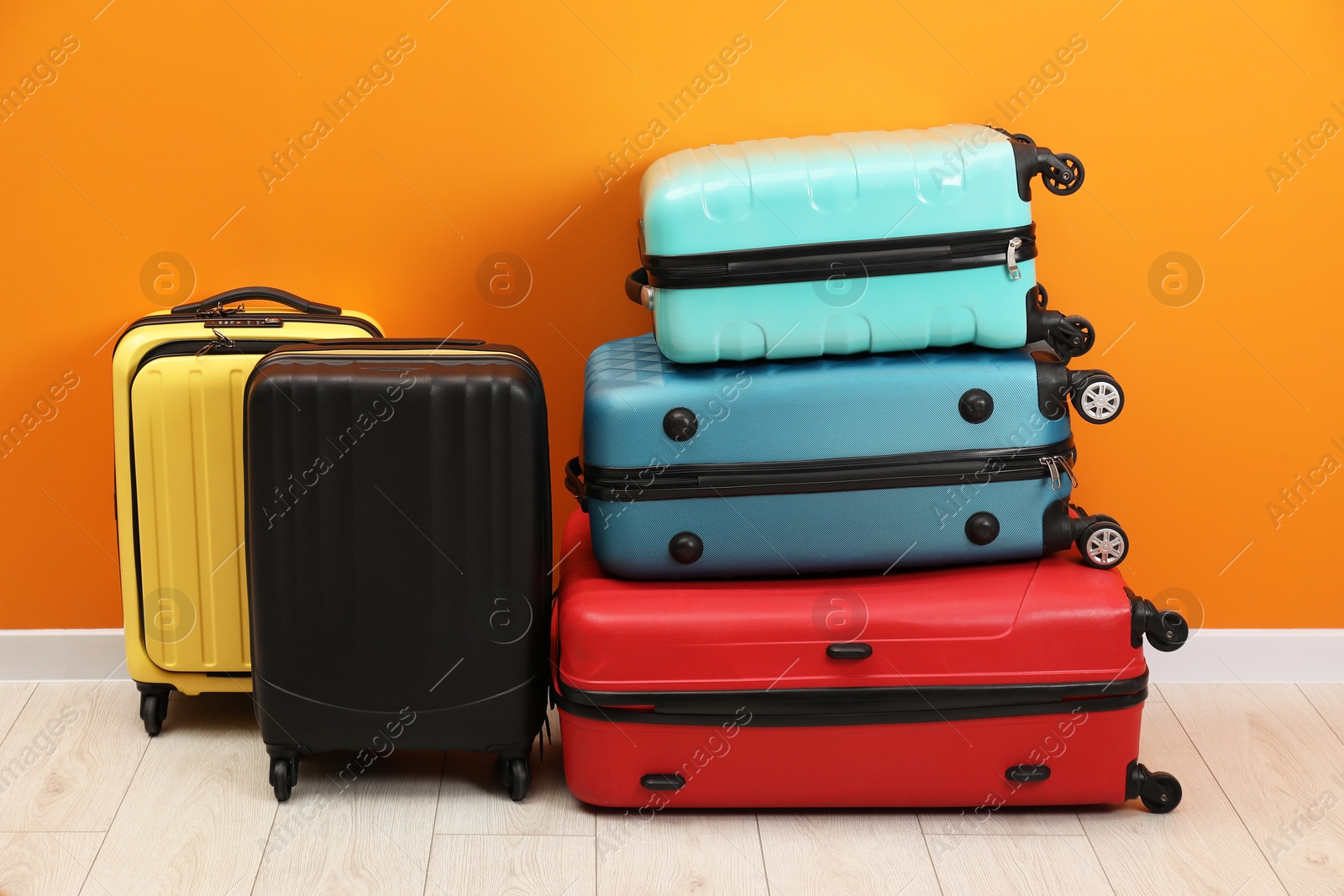 Photo of Many colorful suitcases on floor near orange wall