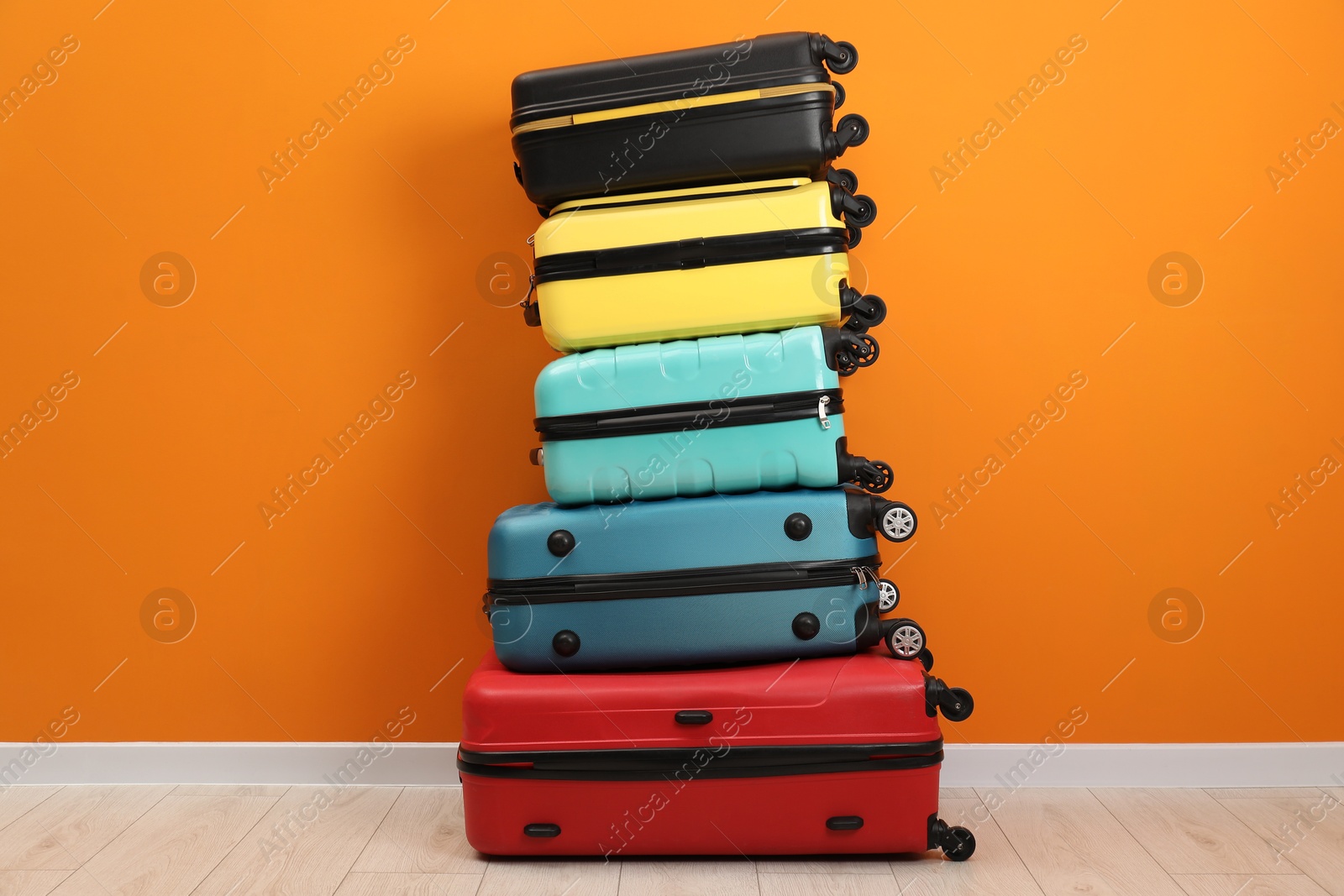 Photo of Stack of colorful suitcases on floor near orange wall