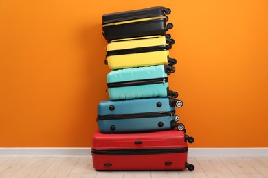 Photo of Stack of colorful suitcases on floor near orange wall