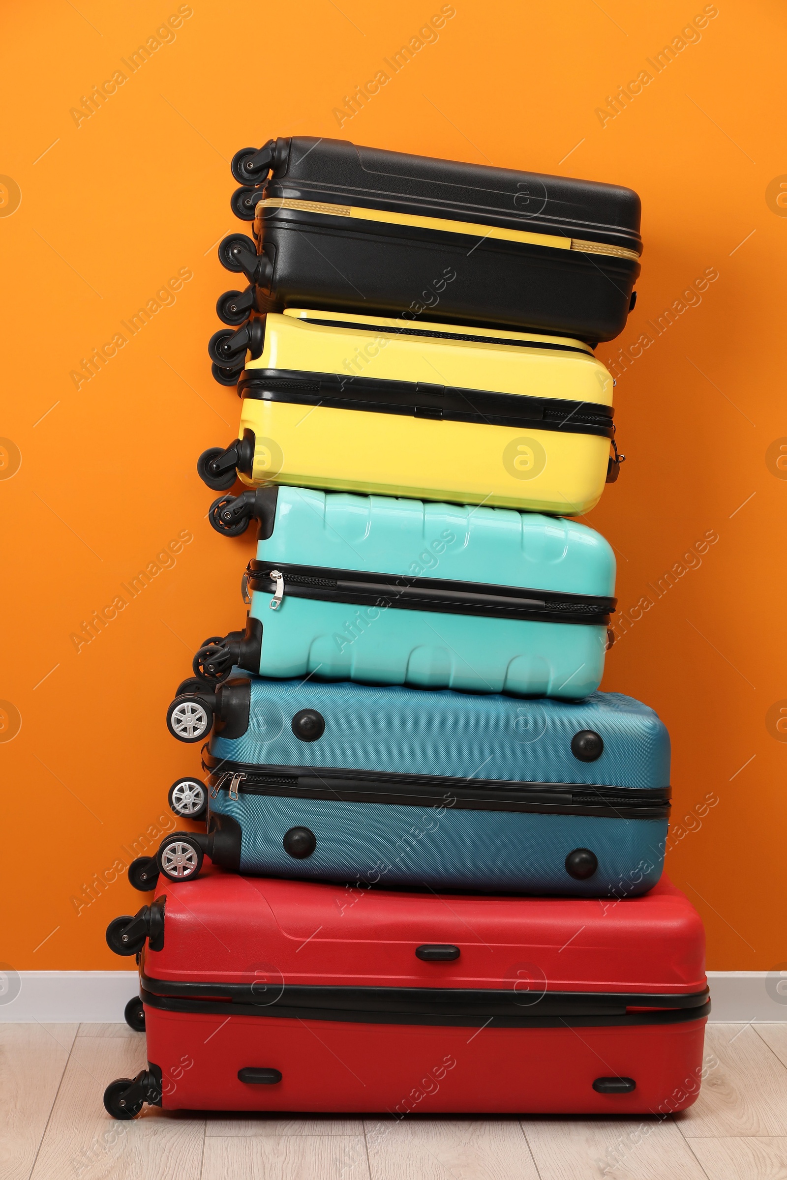 Photo of Stack of colorful suitcases on floor near orange wall