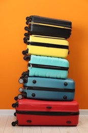 Photo of Stack of colorful suitcases on floor near orange wall