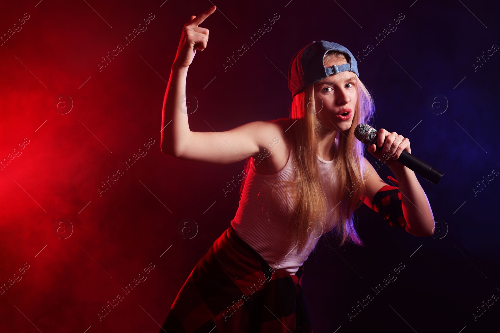 Photo of Talented singer performing on dark background with color lights and smoke