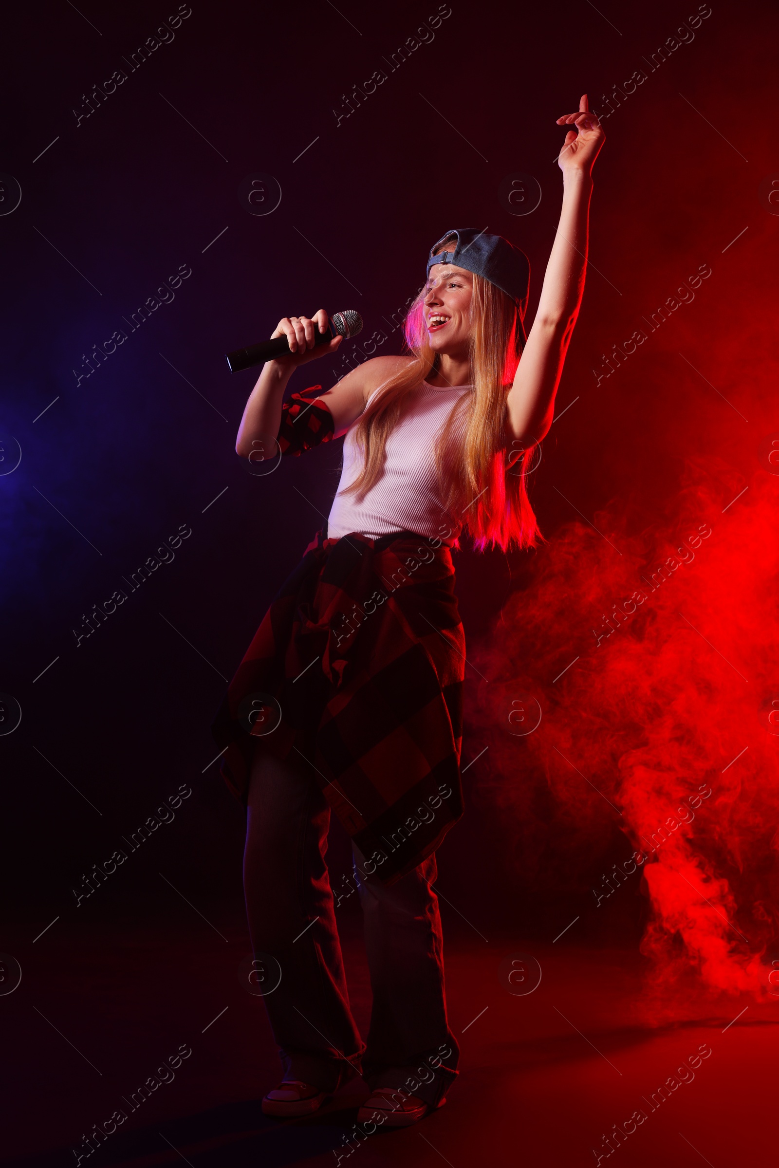 Photo of Talented singer performing on dark background with color lights and smoke