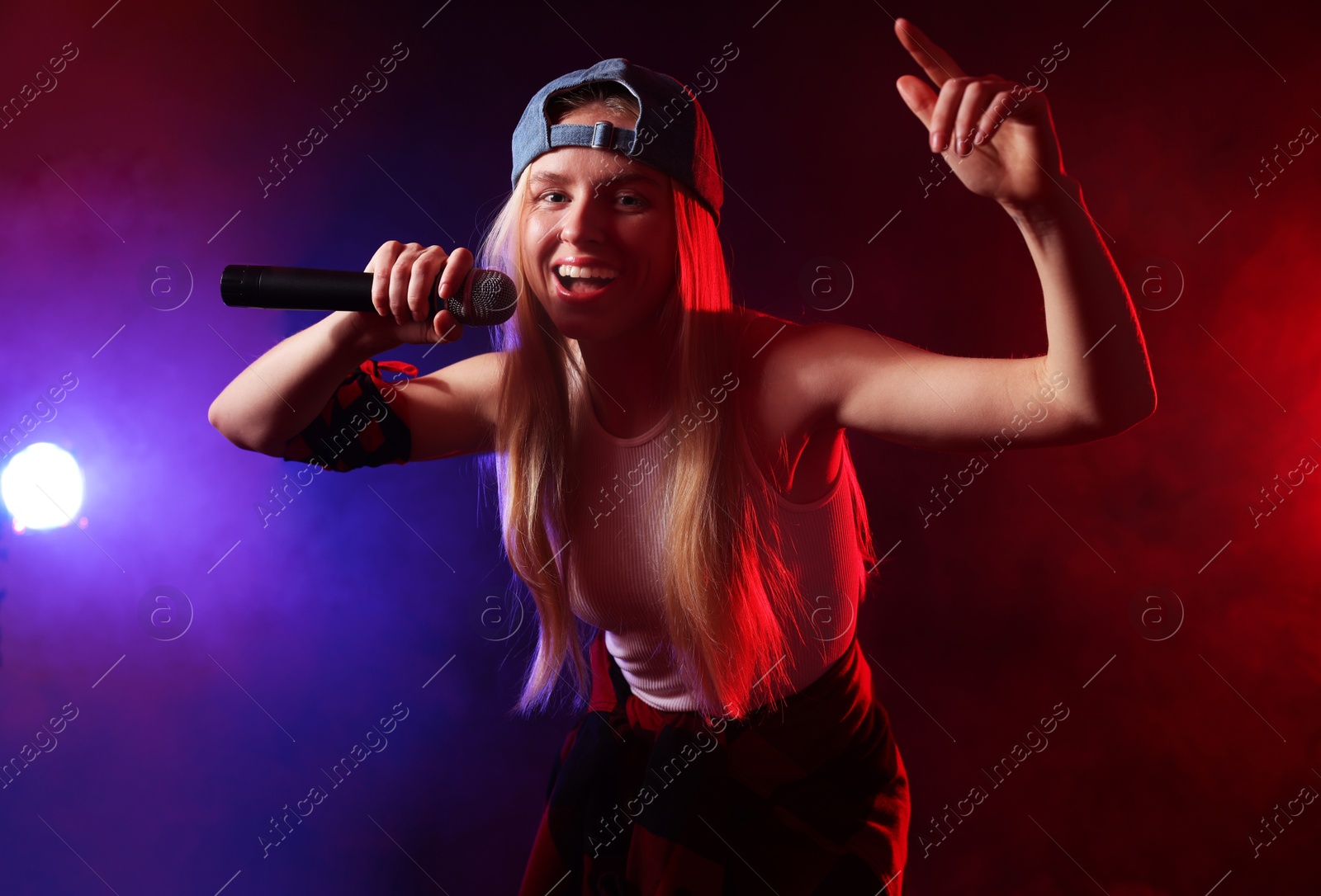 Photo of Talented singer performing on dark background with color lights and smoke