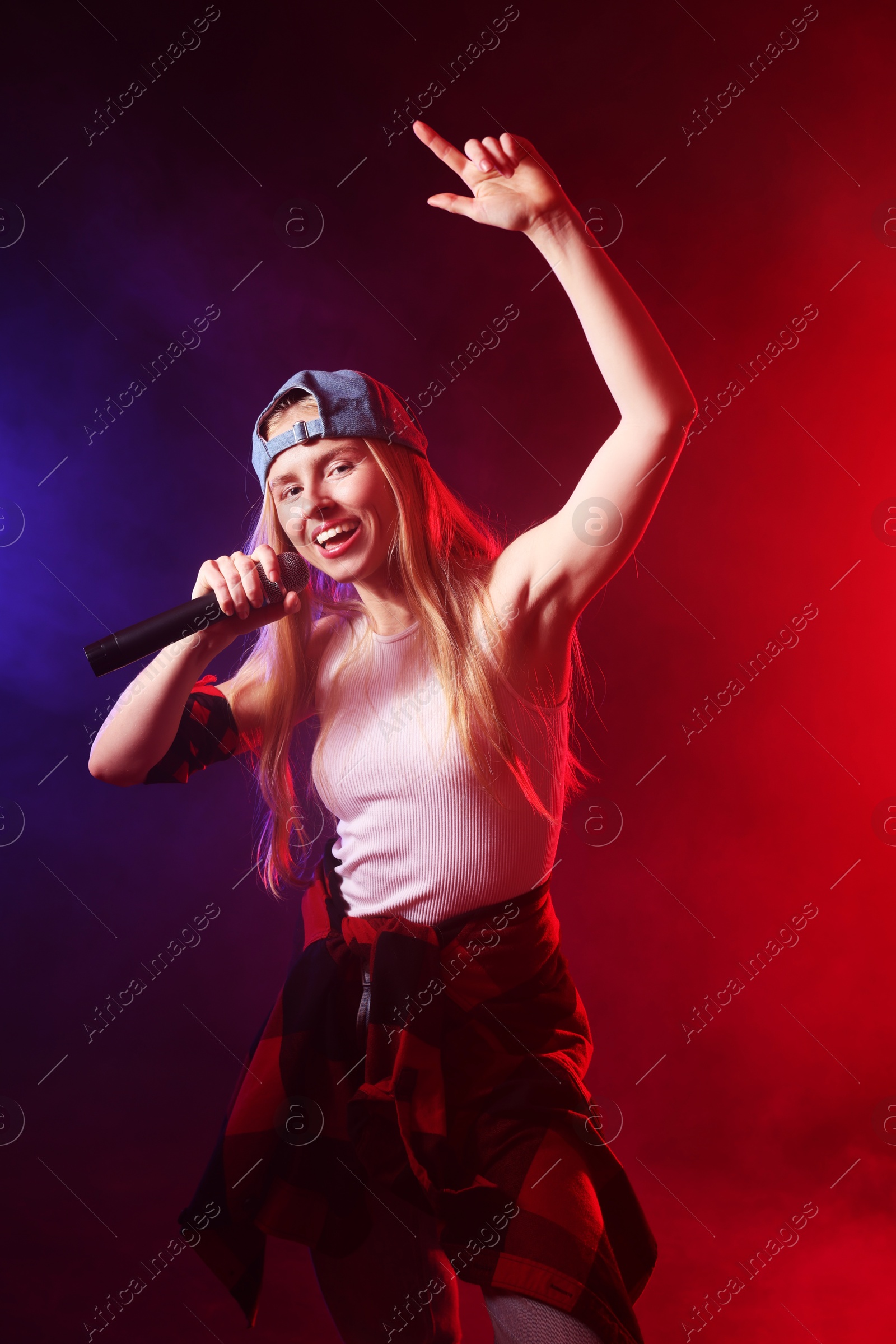 Photo of Talented singer performing on dark background with color lights and smoke