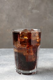 Photo of Refreshing cola with ice cubes in glass on light textured table against grey background, closeup