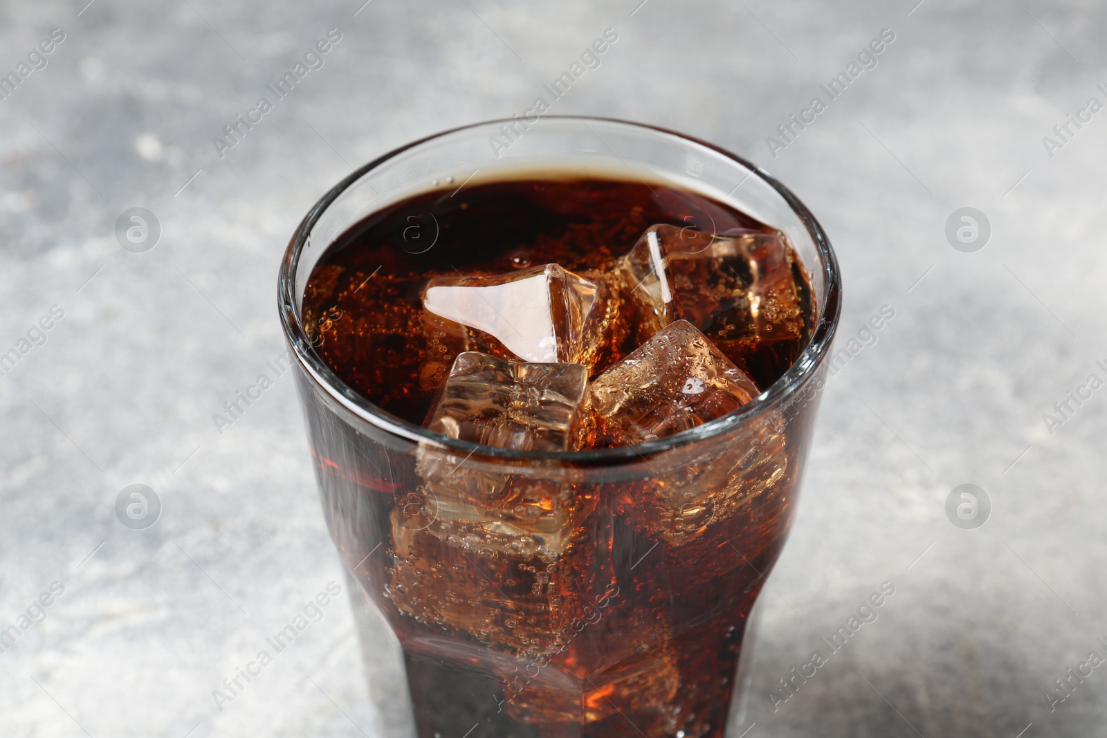 Photo of Refreshing cola with ice cubes in glass on light table, closeup