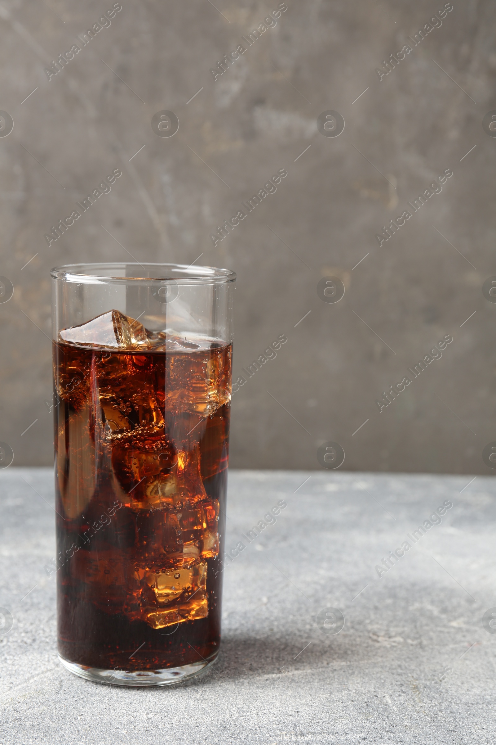 Photo of Refreshing cola with ice cubes in glass on light textured table against grey background, closeup. Space for text