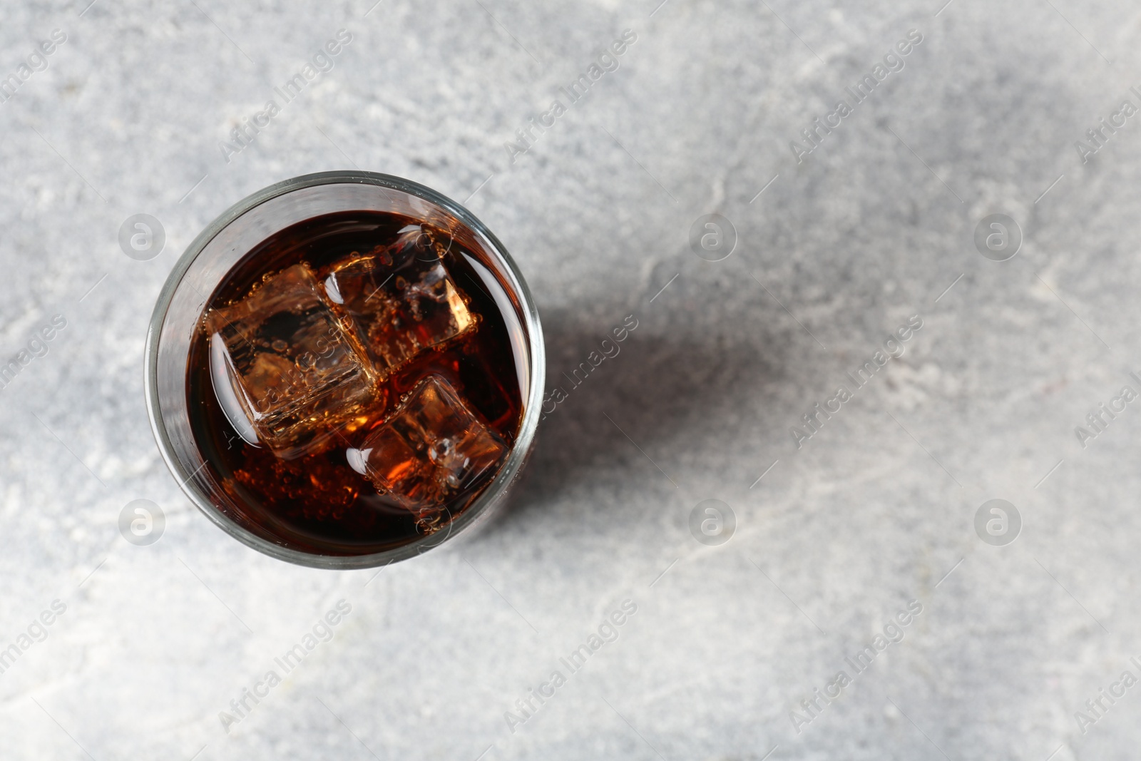 Photo of Refreshing cola with ice cubes in glass on light textured table, top view. Space for text