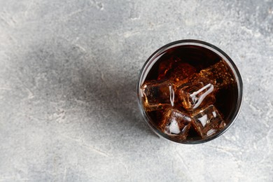 Photo of Refreshing cola with ice cubes in glass on light textured table, top view. Space for text