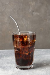 Photo of Refreshing cola with ice cubes and drinking straw in glass on light textured table against grey background, closeup