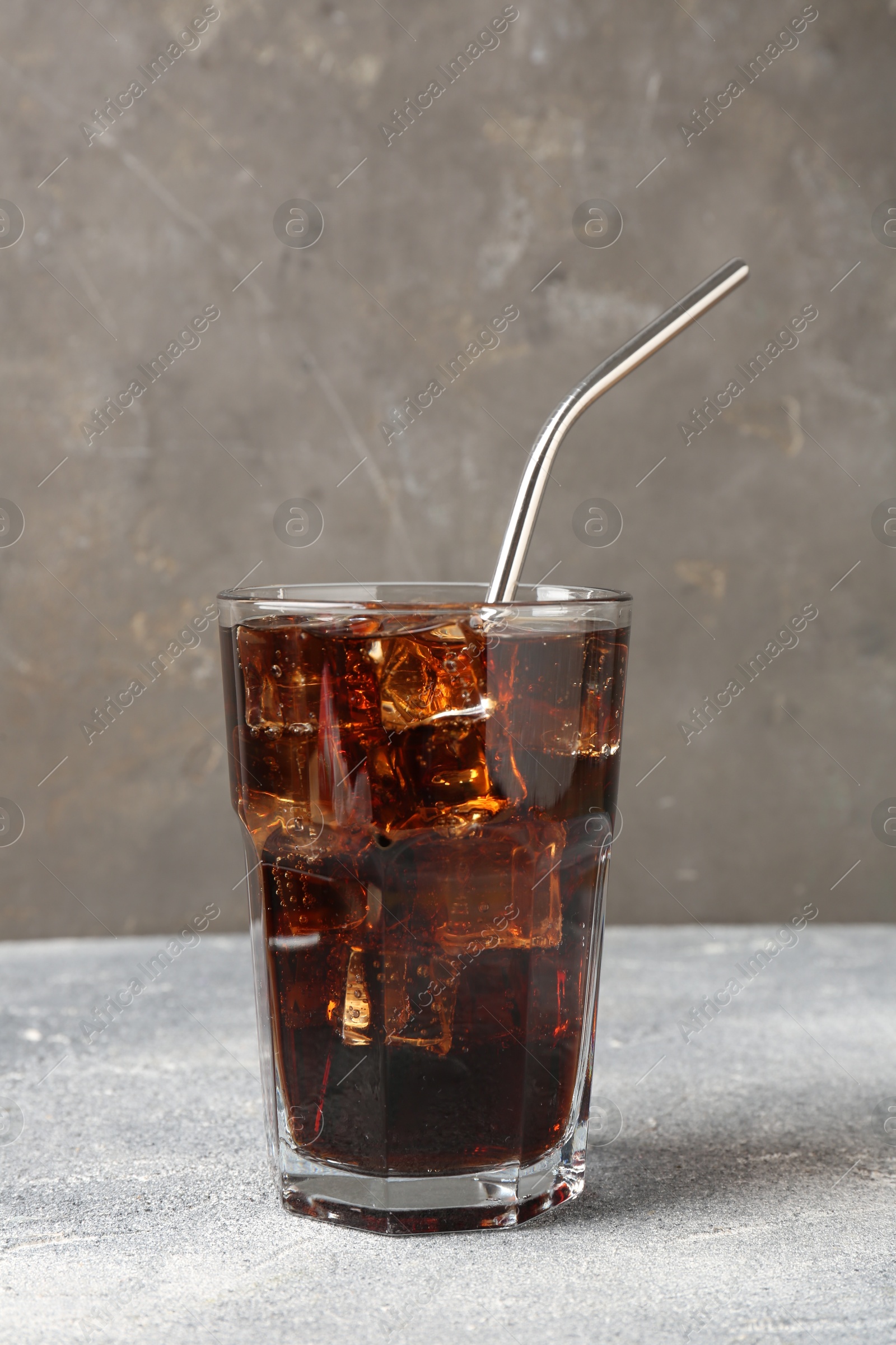 Photo of Refreshing cola with ice cubes and drinking straw in glass on light textured table against grey background, closeup