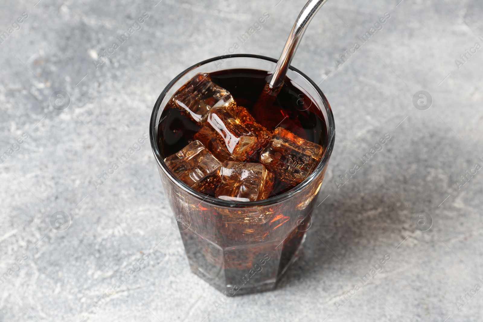 Photo of Refreshing cola with ice cubes and drinking straw in glass on light textured table, closeup