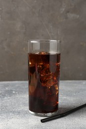 Photo of Refreshing cola with ice cubes in glass and drinking straw on light textured table against grey background, closeup