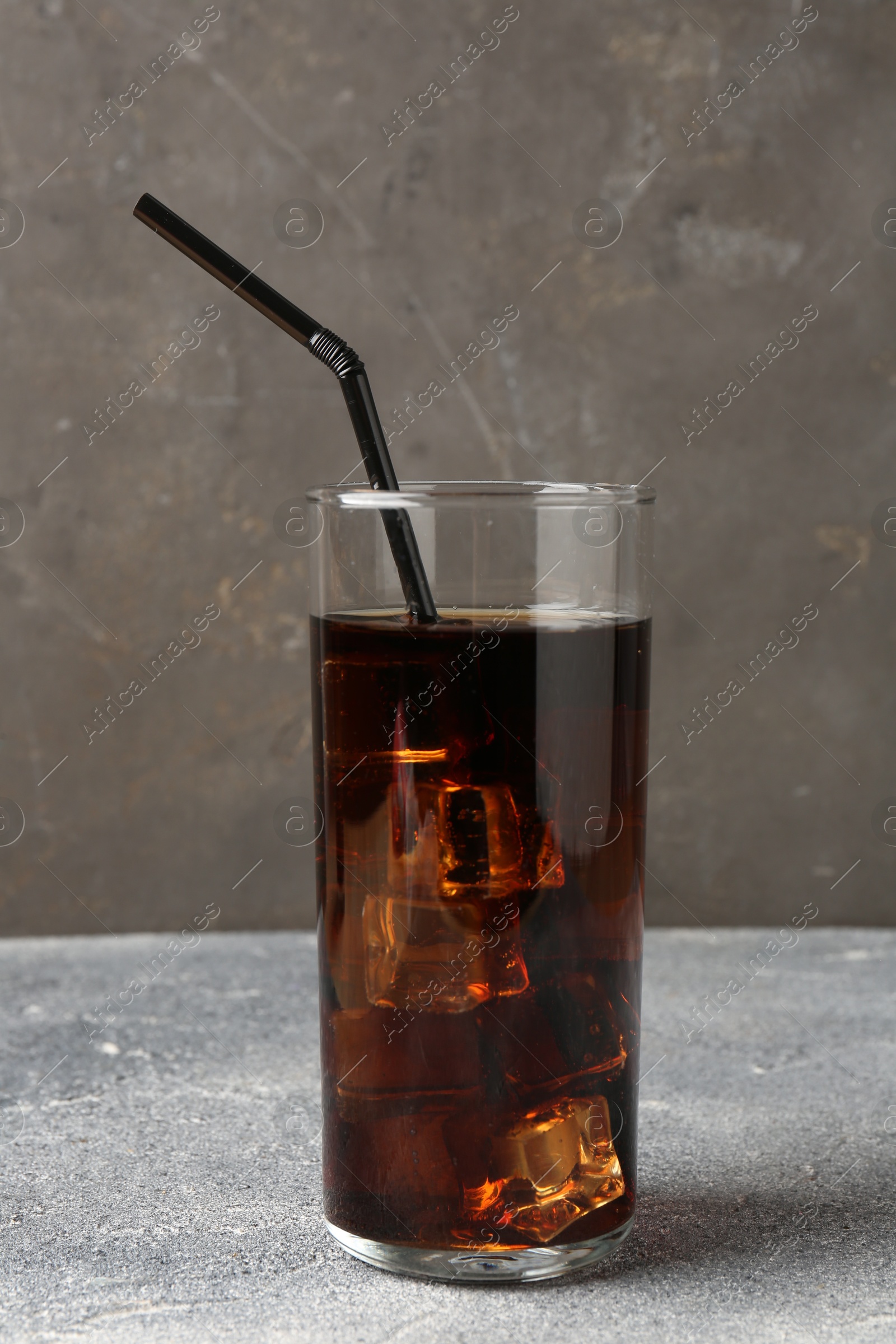 Photo of Refreshing cola with ice cubes and drinking straw in glass on light textured table against grey background, closeup