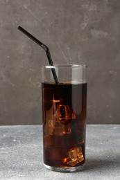 Photo of Refreshing cola with ice cubes and drinking straw in glass on light textured table against grey background, closeup