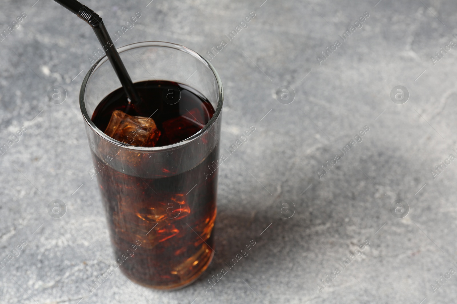 Photo of Refreshing cola with ice cubes and drinking straw in glass on light textured table, closeup. Space for text